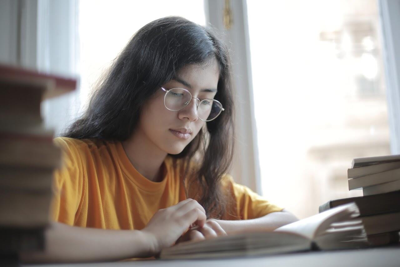 girl with long hair and glasses studying a book